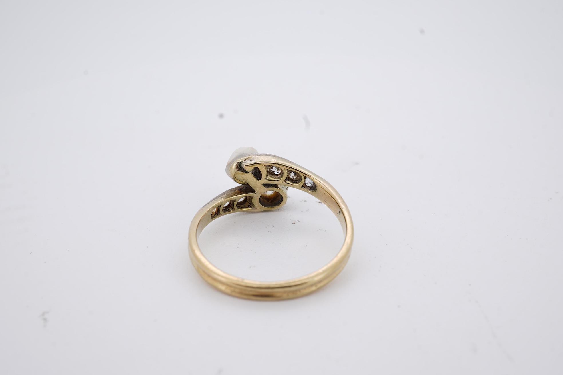 A yellow meta (stamped 18ct) cultured pearl and diamond set crossover ring, with six stone graduated diamond set shoulders, size M, gross weight 2.6 grams (pearl nacre a.f.).